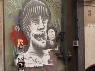 Pisa, İtalya - 16 Ekim 2025 Sokak Sanat Yapıştırıcısı Sarı gözlü ve ağzı açık, kentsel çıkartmalar ve grafiti ile kaplı grotesk bir yüzü gösteren