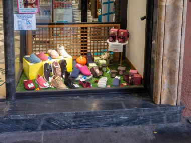 Pisa, İtalya - 16 Ekim 2025 Mağaza vitrininde terlikler ve spor ayakkabıları da dahil olmak üzere renkli ayakkabılar, kozmetik şişeler ve sonbahar satışlarını gösteren bir balkabağı