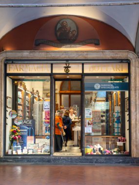 Pisa, İtalya - 16 Ekim 2025 tarihi İtalyan eczane binasını terk eden yaşlı bir kadın, elinde baston ve alışveriş çantası, Avrupa 'daki bir caddede günlük yaşam