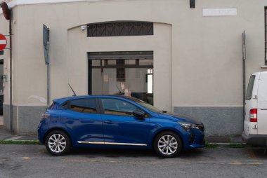 Cremona, İtalya - 2 Ekim 2025 Blue Renault Clio E-TECH hibrit otomobili Avrupa şehir caddesinde park halinde, camında kentsel hareketlilik gösteren bir kişi görülüyor