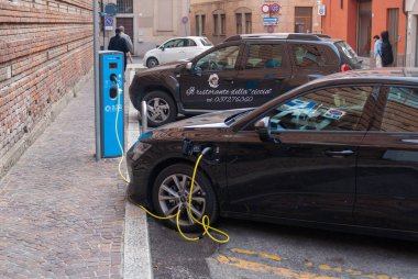 Cremona, İtalya - 2 Ekim 2025 Mavi kamu istasyonunda sarı kablo ile çalışan elektrikli araba şehir caddesinde, sürdürülebilir hareket ve sıfır emisyon teşvik