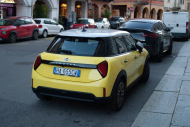 Cremona, İtalya - 2 Ekim 2025 Gösterişli Sarı Mini Cooper EV hareketli bir Avrupa şehir caddesinde park halinde, verimli elektrik hareketliliği, çağdaş hatchback tasarımı ve modaya uygun kentsel flai