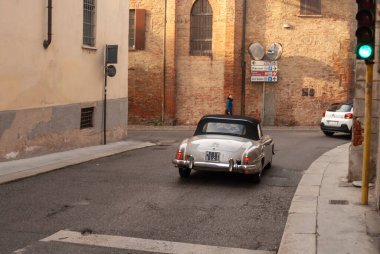 Cremona, İtalya - 2 Ekim 2025 Klasik Mercedes-Benz 190 SL üstü açık araba Avrupa 'da tuğla binalar ve trafik ışıklarıyla kaplı büyüleyici bir caddede süzülerek güneşli havanın tadını çıkarıyor.