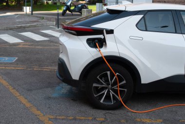 Cremona, İtalya - 2 Ekim 2025 Toyota C-HR turuncu kabloyla elektrik akımı, sıfır emisyonlu kentsel ulaşım ve sürdürülebilir enerji ile bir şehir caddesine park etti..