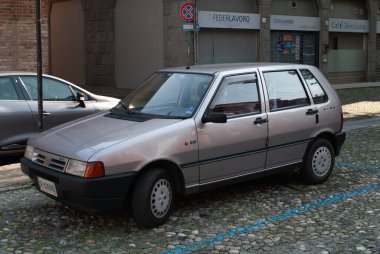 Cremona, İtalya - 2 Ekim 2025 Fiat Uno MKII hatchback büyüleyici bir kaldırım taşı caddesine park edilmiş, arka planda tarihi yapılar, yan profilini gözler önüne seriyor.
