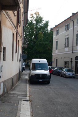 Cremona, İtalya - 2 Ekim 2025 Beyaz Mercedes-Benz Sprinter dağıtım minibüsü dar bir Avrupa caddesinin, arabaların ve arkadaki eski konut binalarının kaldırımına park edilmiş.