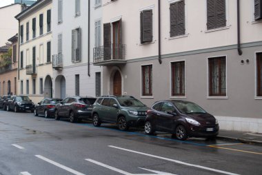 Cremona, İtalya - 2 Ekim 2025 Islak bir iskan caddesine park edilmiş araçlar tarihi Avrupa binalarının yanında bulutlu bir gökyüzünün altında kepenkleri olan