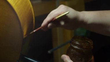 Kalifiye bir zanaatkar kaburgalara hassasiyetle koruyucu cila uyguluyor, hassas çello restorasyonu sırasında karmaşık marangozluk tekniklerini vurguluyor, yavaş çekim