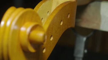Luthier atölyesinde özel aletler ve vernik kullanarak çello tomarını titizlikle hazırlıyor. İşlemin karmaşık detaylarını gösteriyor.