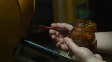 Ahşap çello gövdesine zengin verniği dikkatlice uygulayarak, titiz işçilik ve geleneksel ahşap işçiliği tekniklerini yakın çalışma ortamında vurgulayarak deneyimli bir Luthier uyguladım.