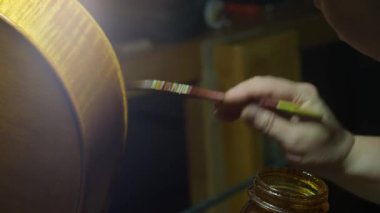 Geleneksel vernikleri ahşap çelloya dikkatlice uygulamak, yakın sanatsal atölye ortamında karmaşık marangozluk tekniklerini vurgulamak.