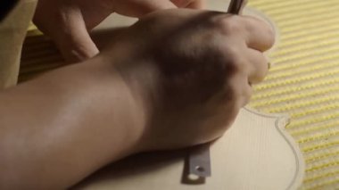 Luthier 'in ellerini titizlikle keman kaplamasında bir delik açarak, geleneksel yavaş çekim atölyesinde hassas ve uzman bir şablon ve kalem kullanarak kapat.