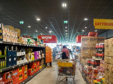 Cremona, İtalya 17 Eylül 2025 Lomb 'daki bütçe dostu bir mağazada içi ürün ve karton kutularla dolu bir market koridorunda dolu bir alışveriş arabasını iten kişi.