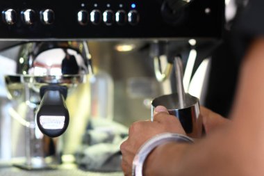 Cremona, İtalya - 21 Temmuz 2025 Barista, yoğun bir sabah boyunca kahve dükkanındaki müşteriler için kaymak gibi bir içecek hazırlayan profesyonel bir espresso makinesi kullanarak metal bir sürahide ustalıkla süt buharlaştırıyor.
