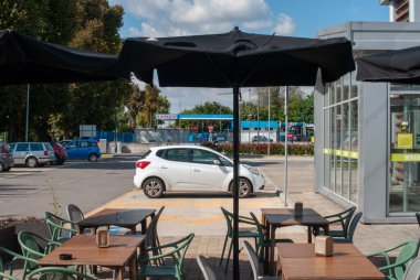 Cremona, İtalya. - 4 Ekim 2025 Banco Fresco süpermarketinin açık hava alanı şemsiyeleri ve boş masaları, yakınlarda park edilmiş arabalar ve arka planda bir Tamoil benzin istasyonu.