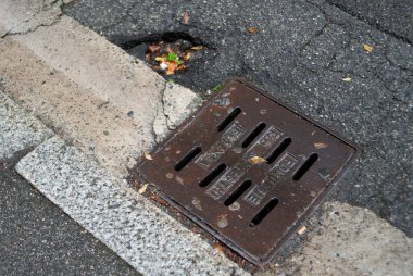 Cremona, İtalya. - 4 Ekim 2025 Paslı demir rögar kapağını, beton kaldırımı ve yanında düşmüş yaprakları olan bir sokağın kaba desenli asfaltına yerleştirin.