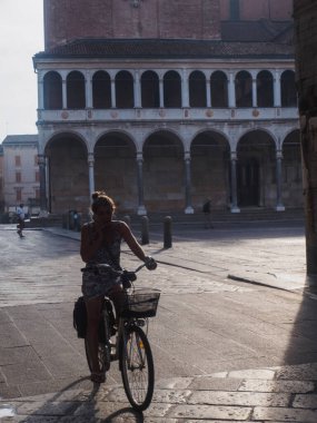 Cremona, İtalya. 13 Ağustos 2025. Genç turist, İtalya 'nın Cremona şehrinde bisiklet sürüyor. Lombardy' de, arkada da Loggia dei Militi sarayı var.
