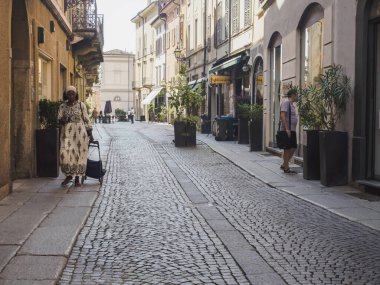 Cremona, İtalya 13 Ağustos 2025 Afrikalı bir kadın, güneşli bir yaz gününde, İtalya 'nın Cremona şehrinde bir alışveriş arabasıyla bir kaldırım taşı caddesinde yürüyor.