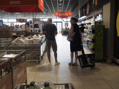 Cremona, İtalya 11 Ağustos 2025 Süpermarket koridorunda duran müşteriler raflardan ve tanıtımlardan alışveriş arabası ve sepeti, alışveriş yaşam tarzı konsepti olan ürünleri seçiyorlar.