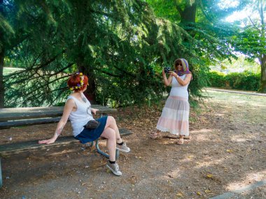 Parkta güneşli bir günün tadını çıkaran iki kadın. Biri diğerinin fotoğrafını çekiyor.