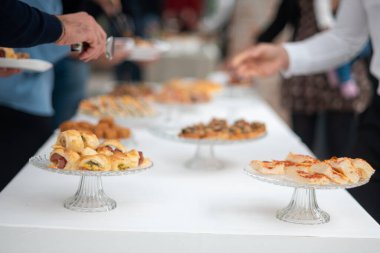 Konuklar özel bir etkinlikte lezzetli aperatifler ve parmak yiyeceklerle dolu beyaz bir masanın etrafında toplanıp canlı bir açık büfe sahnesi yaratıyorlar.
