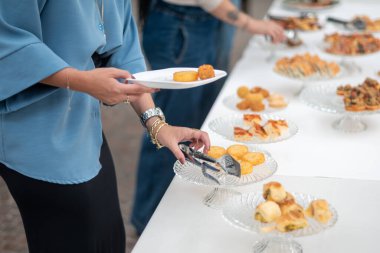 Misafirler, çeşitli aperatifler ve çeşitli ikramlar sergilenen özel bir etkinlik sırasında zarif bir açık büfe masasından, sosyal toplantılar için ideal cam tabaklar üzerinde sanatsal olarak sunulan lezzetli yemekleri seçiyorlar.