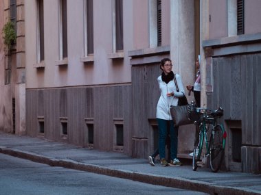 Cremona, İtalya 27 Eylül 2025 kaldırımda bisiklet süren genç bir kadın, kapı eşiğinde bir insanla konuşuyor, Cremona 'da günlük hayatı yakalıyor.