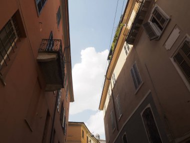 Cremona, İtalya 11 Eylül 2025. İki eski çok katlı bina, pencereleri, balkonları ve parlak mavi gökyüzünün altında panjurları olan bir sokak kanyonu oluşturuyorlar.