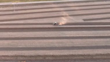 Bir tarım traktörünün kuru toprağı sürdüğü ve geniş bir tarlada izler bıraktığı, toprağı yeni bir hasat mevsimi için hazırlarken toz bulutlarını tekmelediği yüksek hava manzarası.