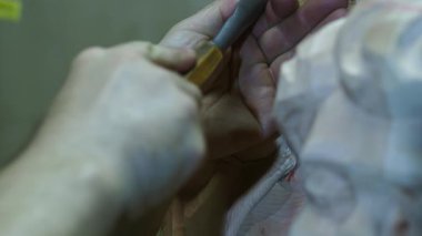 Profesyonel ahşap işçiliğinin hassasiyetini ve sanatını gözler önüne seren ahşap bir heykele detaylı bir tasarım yapmak için geleneksel bir keski kullanan yetenekli bir zanaatkârın ellerini kapatın.