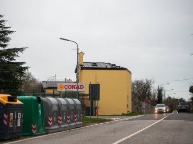 Trieste, İtalya - 21 Kasım 2025 Conad süpermarketi İtalya Slovenya sınırı yakınlarındaki bir yolda, geri dönüşüm kutuları cadde ve arabaların bulutlu bir günde geçtiği,
