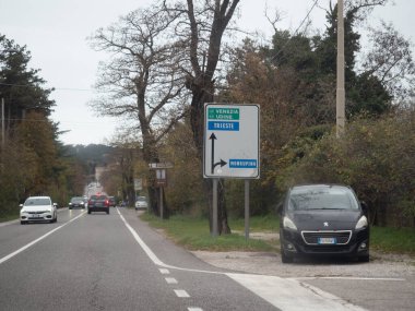 Trieste, İtalya - İtalya - 21 Kasım 2025 Slovenya sınırındaki bir köy yolunda duran, farklı şehir ve kasabaların yönlerini gösteren, gezen ve park eden arabaları gösteren tabela