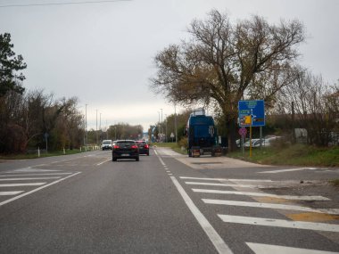 Trieste, İtalya - 21 Kasım 2025 İtalya sınırına doğru giden araçlar, İtalya ve Slovenya 'da bulutlu bir gökyüzü altında duracakları yerleri gösteren bir yön işaretinden geçiyor.
