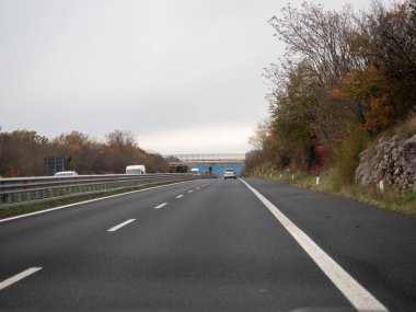 Friuli, İtalya 21 Kasım 2025 İtalya 'da A4 otoyolunda, bulutlu gökyüzüne karşı asfalt karayolunda seyahat eden araçlar. İleri hareket ve ulaşım kavramı