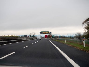 Friuli, İtalya 21 Kasım 2025 A4 otoyolu bulutlu gökyüzünün altında uzak Alplere doğru giden boş şeritler boyunca trafiği yönlendiren değişken bir mesaj işareti ile