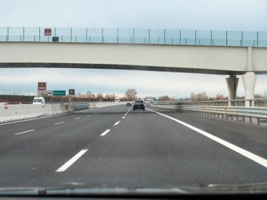 Friuli, İtalya 21 Kasım 2025 Bir üst geçidin altındaki A4 otostradında ilerleyen bulutlu, boş bir otoyolda yön işaretleri ile birlikte