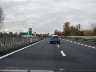 Friuli, İtalya 21 Kasım 2025 Bulutlu bir gökyüzünün altında İtalyan A4 otoyolunda yavaşlayan araba ve kamyonlar, sonbahar ağaçlarıyla kaplı şeritler boyunca uzanan sıkışıklık