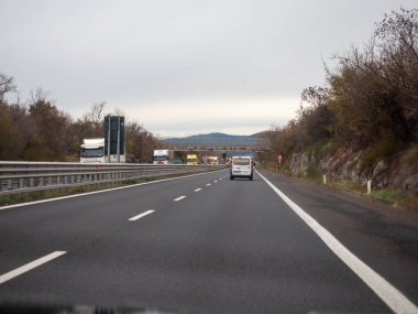 Friuli, İtalya 21 Kasım 2025 Friuli Venezia Giulia 'da arabaları ve kamyonları düz asfalt, yuvarlanan tepeler ve bulutlu gökyüzü boyunca hızla giden uzak bir üstgeçit dinamik bir yolculuk çerçevesi oluşturan
