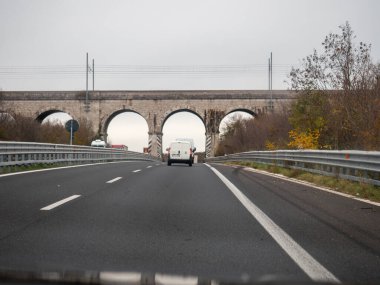 Friuli, İtalya 21 Kasım 2025 Büyük bir otoyolda giden bir arabadan eski bir tren köprüsüne doğru giden, ulaşım altyapısını birbirine bağlayan bir otoyol.