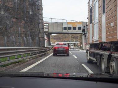 Friuli, İtalya 21 Kasım 2025 İtalya 'nın A4 otoyolunda ön cam manzarası, taş bir duvarı geçen araçlar ve bulutlu bir günde tepeden karşıya geçen araçlar