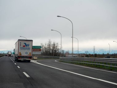 Friuli, İtalya 21 Kasım 2025 Bir İtalyan otoyolu üzerinde bir çıkışa doğru giden kamyon, Palmanova ve Grado için yol işaretleri, uzak dağlar