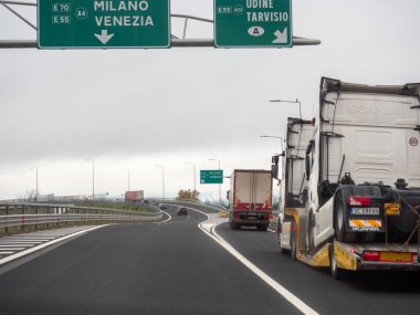 Friuli, İtalya 21 Kasım 2025 A4 İtalyan otoyolu boyunca giden ağır kamyonlar, Milano ve Venezia 'ya giden yol tabelalarını geçerek nakliye aracını sembolize ediyor.