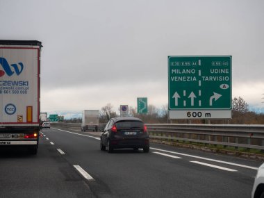 Friuli, İtalya 21 Kasım 2025 Çok şeritli bir otoyolda seyahat eden araçlar, çeşitli İtalyan şehirlerine giden yolu gösteren büyük yeşil bir yol tabelasını geçtiler.