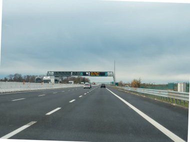 Friuli, İtalya 21 Kasım 2025 Bulutlu gökyüzü altında arabalar ve kamyonlarla otoyol A4, asfalt yolda ödeme seçeneklerini gösteren kirişlere elektronik gişe işareti