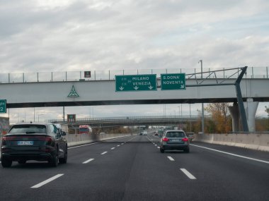 Venedik, İtalya 21 Kasım 2025 Veneto, İtalya yakınlarındaki otostrada A4 işaretleri altında seyir halindeki araçlar açık otoyolu ve yön rehberliğini çerçeveleyen bulutlu gökyüzü