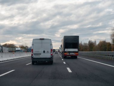 Venedik, İtalya 21 Kasım 2025 İtalyan Autostrada A4 üzerindeki araçlar, bulutlu bir gökyüzü, hareket ve altyapı altında birden fazla şeritte seyahat eden beyaz teslimat aracı ve kargo kamyonu