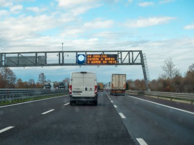 İtalya, Venedik, 21 Kasım 2025 İtalya 'da A4 otoyolu üzerinde seyahat eden araçlar, kış sürüş gereksinimlerini gösteren değişken bir mesaj işareti göstermektedir.