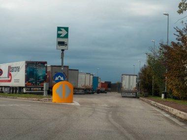 Venedik, İtalya 21 Kasım 2025 Nakliye kamyonları İtalyan otoyolunda bir servis alanına park ettiler. Yeşil tabela kamyon yönünü ve lojistik merkezini gösteriyor.