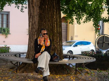 Bir kadın, şehir bankında dinlenirken cep telefonuyla arama yapıyor.