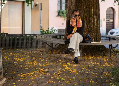 Sonbahar boyunca parkta bankta oturan, cep telefonuyla konuşan olgun siyahi bir kadın.